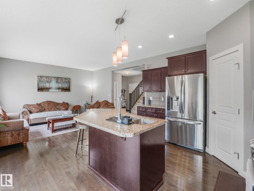 Wood-finish flooring throughout, kitchen island with stone countertop, stainless steel refrigerator, recessed lighting, and a contemporary pendant fixture - 1478 37B Avenue Nw, Edmonton, AB - Indoor Photo Showing Kitchen