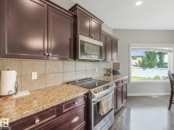 Kitchen featuring dark wood cabinetry, light-toned tiled backsplash, speckled stone countertops, and stainless steel appliances - 