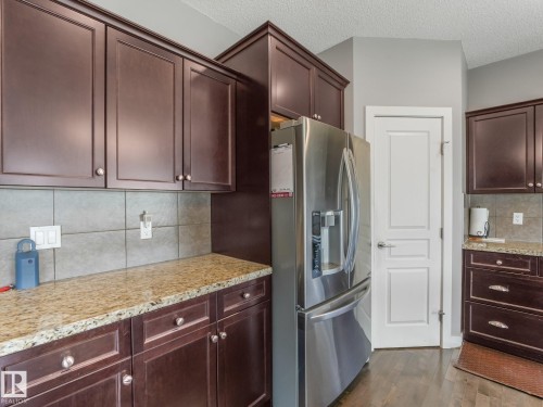 Rich wood-finish cabinetry with contrasting hardware, light-toned tiled backsplash, and stone-finish countertops - 1478 37B Avenue Nw, Edmonton, AB - Indoor Photo Showing Kitchen