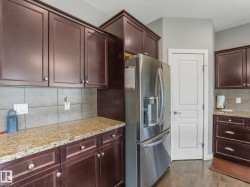 Rich wood-finish cabinetry with contrasting hardware, light-toned tiled backsplash, and stone-finish countertops - 