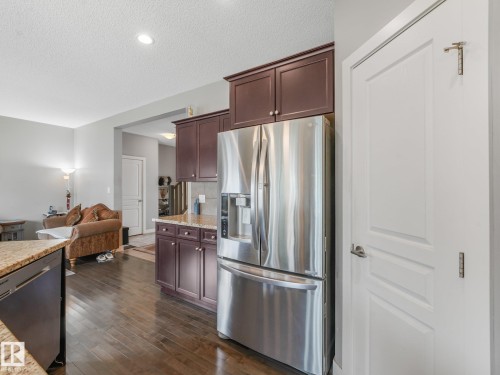 Kitchen featuring dark wood cabinetry, stainless steel refrigerator, granite countertops, and wood-finish flooring - 1478 37B Avenue Nw, Edmonton, AB - Indoor Photo Showing Kitchen