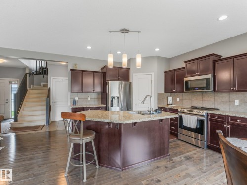 Kitchen featuring wood-finish flooring, dark wood cabinetry, stainless steel appliances, a kitchen island with a stone-finish countertop, and pendant lighting - 1478 37B Avenue Nw, Edmonton, AB - Indoor Photo Showing Kitchen With Upgraded Kitchen