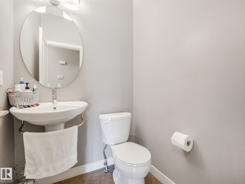 Pedestal sink with chrome faucet, circular wall mirror, and two-bulb vanity light fixture - 1478 37B Avenue Nw, Edmonton, AB - Indoor Photo Showing Bathroom