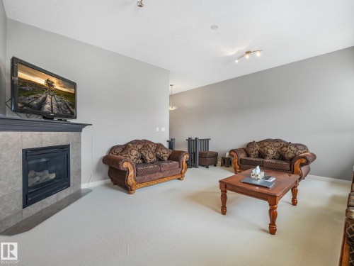 Tiled fireplace with a dark mantle, light neutral wall paint, and white carpet flooring - 1478 37B Avenue Nw, Edmonton, AB - Indoor Photo Showing Living Room With Fireplace