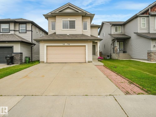 Beige siding exterior with a light-colored garage door, concrete driveway, and a paved brick border - 1478 37B Avenue Nw, Edmonton, AB - Outdoor With Facade