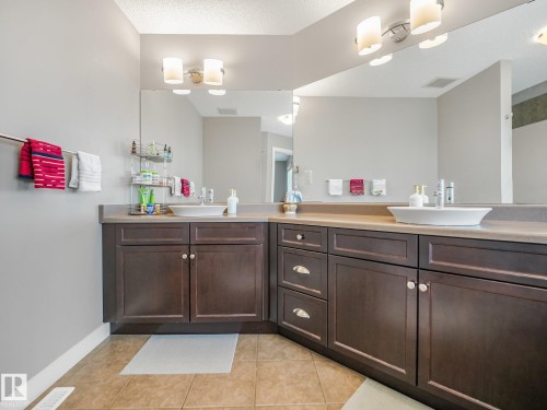 Dual vessel sinks, dark wood-finish cabinetry, extensive countertop space, large wall-mounted mirrors, and tiled flooring - 1478 37B Avenue Nw, Edmonton, AB - Indoor Photo Showing Bathroom