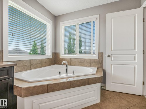Corner soaking tub with tile surround, dual windows, and built-in cabinetry - 1478 37B Avenue Nw, Edmonton, AB - Indoor Photo Showing Bathroom
