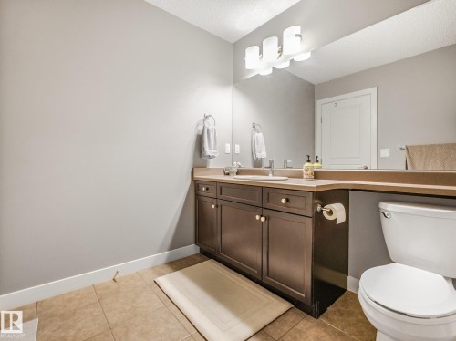 Bathroom featuring a brown vanity with integrated sink, a large wall-mounted mirror, overhead vanity lighting, and tiled flooring - 1478 37B Avenue Nw, Edmonton, AB - Indoor Photo Showing Bathroom