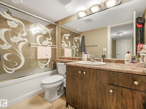 Tub/shower combination with decorative glass sliding doors, wood-finish vanity with an integrated sink, and a large wall-mounted mirror - 1478 37B Avenue Nw, Edmonton, AB - Indoor Photo Showing Bathroom