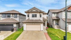 Two-story residence featuring light-toned siding, a front-facing attached garage, and a peaked roofline - 