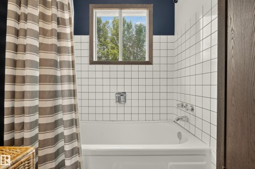Bathtub with white square tile surround, chrome fixtures, and a framed window - 264 Beach Avenue, Rural Barrhead County, AB - Indoor Photo Showing Bathroom