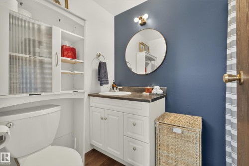 White vanity with integrated sink, dark countertop, circular mirror, and wall-mounted vanity lighting - 264 Beach Avenue, Rural Barrhead County, AB - Indoor Photo Showing Bathroom