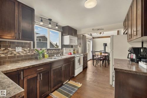 Kitchen featuring dark wood-finish cabinetry, a subway tile backsplash with mosaic accents, and a dual-basin stainless steel sink - 264 Beach Avenue, Rural Barrhead County, AB - Indoor Photo Showing Kitchen With Double Sink