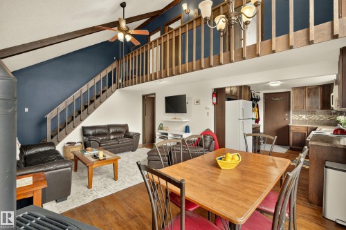 Vaulted ceiling with exposed beams, wood-finish flooring, staircase to upper level, and a kitchen with wood cabinetry and tile backsplash - 264 Beach Avenue, Rural Barrhead County, AB - Indoor