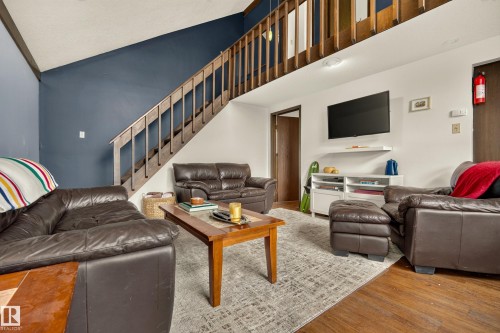 Open-concept living area with a vaulted ceiling, wood-finish flooring, and a natural wood staircase - 264 Beach Avenue, Rural Barrhead County, AB - Indoor Photo Showing Living Room