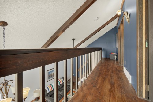 Wood-finish flooring, exposed ceiling beams, white railing spindles, and a dark wood-finish handrail - 264 Beach Avenue, Rural Barrhead County, AB - Indoor Photo Showing Other Room