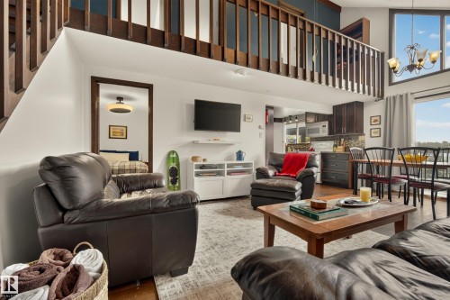 Two-story living area with wood-finish flooring, a lofted space with wood railing, large windows, and a built-in kitchen - 264 Beach Avenue, Rural Barrhead County, AB - Indoor Photo Showing Living Room
