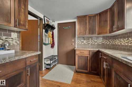 Wood-finish flooring, dark wood cabinetry, granite-look countertops, and a subway tile backsplash with mosaic accents - 264 Beach Avenue, Rural Barrhead County, AB - Indoor Photo Showing Kitchen