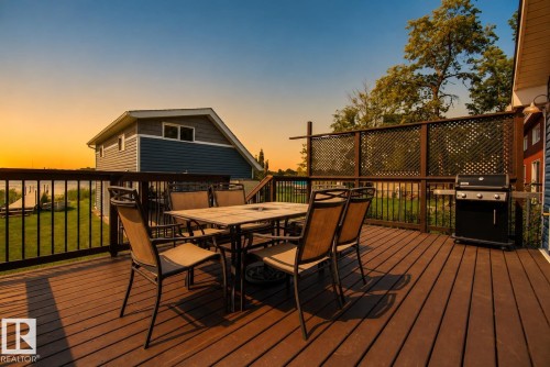 Expansive wood-finish deck with black metal railings, lattice privacy screen, and exterior wall sconces - 264 Beach Avenue, Rural Barrhead County, AB - Outdoor With Deck Patio Veranda With Exterior