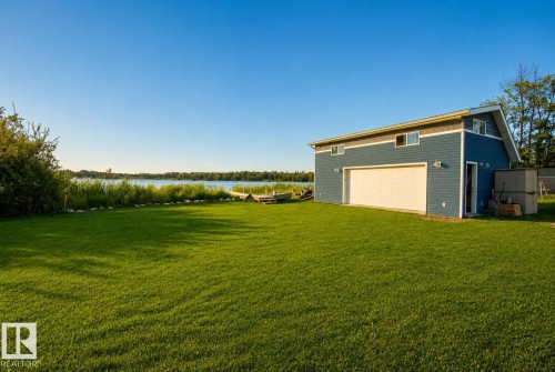 Expansive lawn area with a two-story structure featuring blue siding and a large garage door - 264 Beach Avenue, Rural Barrhead County, AB - Outdoor
