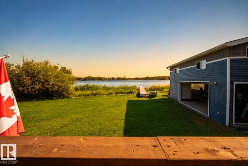 Waterfront property featuring a private dock, expansive green space, mature landscaping, and a two-story residence with blue siding and an attached garage - 264 Beach Avenue, Rural Barrhead County, AB - Outdoor With View