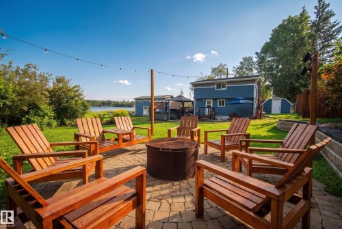 Paver patio with a central fire pit, string lighting, and direct access to a grassy yard - 264 Beach Avenue, Rural Barrhead County, AB - Outdoor With Deck Patio Veranda