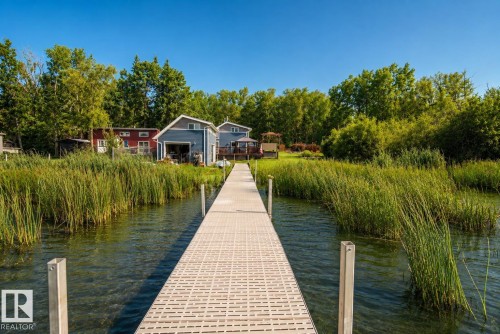 Dock extending into a body of water, surrounded by tall reeds, mature trees, and a clear blue sky - 264 Beach Avenue, Rural Barrhead County, AB - Outdoor With Body Of Water