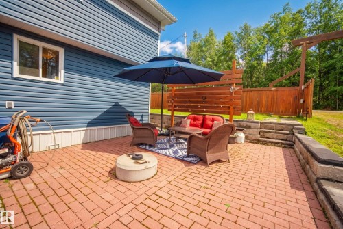 Brick paver patio with a tiered retaining wall, horizontal wood privacy screen, and blue horizontal siding - 264 Beach Avenue, Rural Barrhead County, AB - Outdoor With Deck Patio Veranda With Exterior