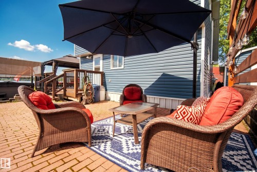 Brick paver patio with a decorative area rug and adjacent wood-built deck - 264 Beach Avenue, Rural Barrhead County, AB - Outdoor With Deck Patio Veranda With Exterior
