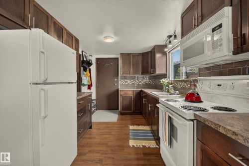Kitchen featuring wood-finish flooring, dark wood cabinetry, a built-in microwave, and a window above the sink - 264 Beach Avenue, Rural Barrhead County, AB - Indoor Photo Showing Kitchen