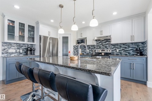 Kitchen featuring a central island with countertop, stainless steel appliances, a tile backsplash, two-tone cabinetry, and wood-finish flooring - 76 Dunlop Wynd, Leduc, AB - Indoor Photo Showing Kitchen With Stainless Steel Kitchen With Upgraded Kitchen