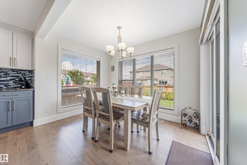 Light wood-finish flooring, white walls, two-tone cabinetry, a mosaic tile backsplash, and a sliding glass door - 76 Dunlop Wynd, Leduc, AB - Indoor Photo Showing Dining Room