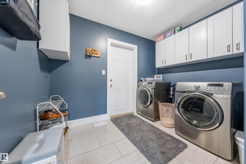 Utility room with light-toned tile flooring, overhead white cabinetry, and a white entry door - 76 Dunlop Wynd, Leduc, AB - Indoor Photo Showing Laundry Room