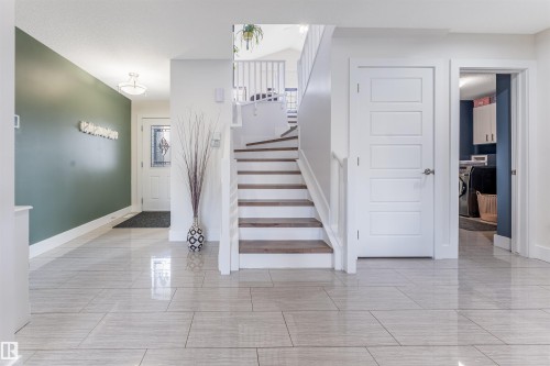 Spacious entry with large format tile flooring, a curved staircase with wood-finish treads, and a paneled entry door - 76 Dunlop Wynd, Leduc, AB - Indoor Photo Showing Other Room