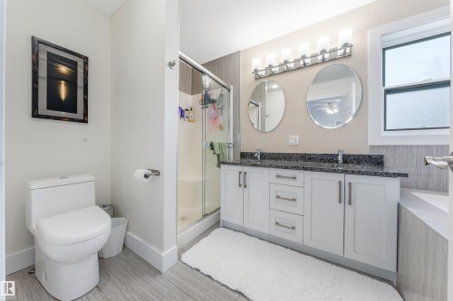 Dual vanity with white cabinetry, dark stone-finish countertop, and two round mirrors - 76 Dunlop Wynd, Leduc, AB - Indoor Photo Showing Bathroom
