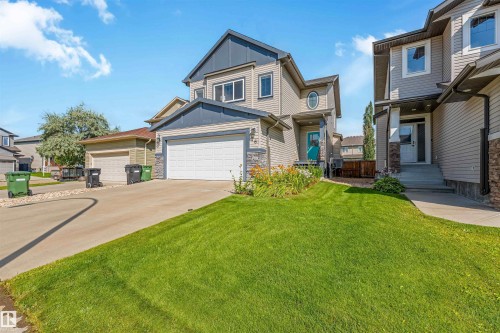 Two-story exterior with siding and stone accents, attached two-car garage, concrete driveway, and a front lawn with established landscaping - 76 Dunlop Wynd, Leduc, AB - Outdoor