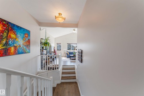 Wood-finish flooring leading to a split-level design, featuring white railings and a prominent overhead light fixture - 76 Dunlop Wynd, Leduc, AB - Indoor Photo Showing Other Room