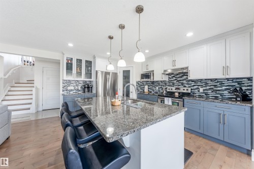 Kitchen featuring a large island with stone countertop, stainless steel appliances, a mosaic tile backsplash, and two-tone cabinetry - 76 Dunlop Wynd, Leduc, AB - Indoor Photo Showing Kitchen With Stainless Steel Kitchen With Double Sink With Upgraded Kitchen