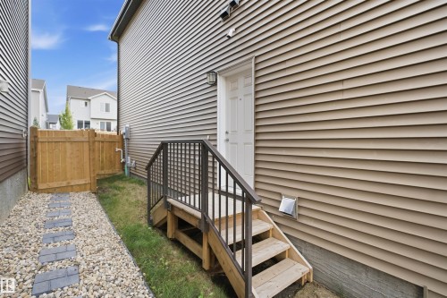 Exterior siding with a white door, wood stairs, and metal railings - 3877 Chrustawka Place Sw, Edmonton, AB - Outdoor