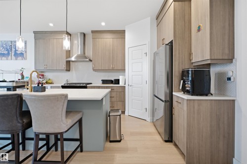 Modern kitchen featuring wood-finish cabinetry, stainless steel appliances, white countertops, and light wood-finish flooring - 3877 Chrustawka Place Sw, Edmonton, AB - Indoor Photo Showing Other Room
