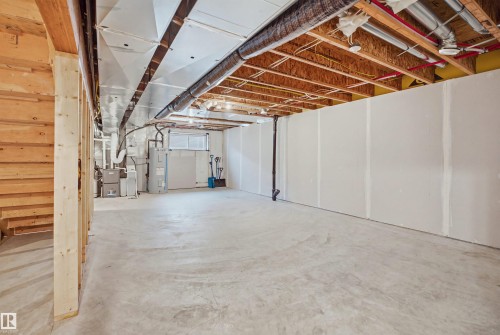 Unfinished basement space featuring exposed wood framing, concrete flooring, and partial drywall installation - 3877 Chrustawka Place Sw, Edmonton, AB - Indoor Photo Showing Basement