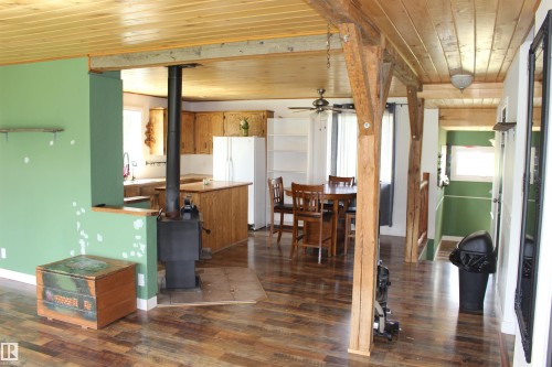 Wood-finish flooring throughout, exposed wood beam ceiling, wood-burning stove, and a kitchen featuring wood cabinetry - 49480 Rge Rd 41, Rural Leduc County, AB - Indoor