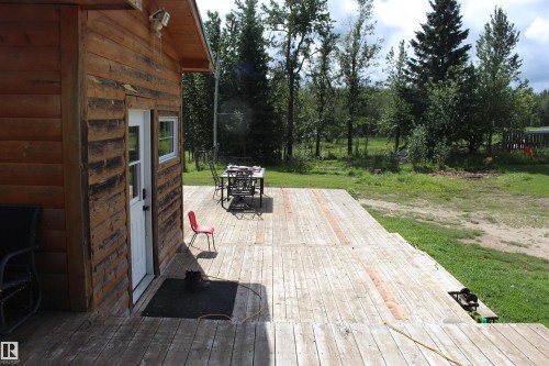 Expansive wood deck with stairs, featuring a side entrance with a white door and window, all set against a backdrop of mature trees - 49480 Rge Rd 41, Rural Leduc County, AB - Outdoor With Deck Patio Veranda