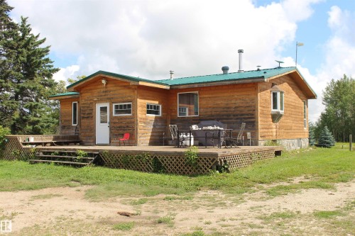 Wood-finish siding exterior featuring a green metal roof, multiple windows, and an expansive outdoor deck - 49480 Rge Rd 41, Rural Leduc County, AB - Outdoor With Deck Patio Veranda