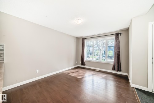 Living area featuring expansive front-facing window, dark wood-finish flooring, light neutral paint, white baseboards, and a semi-flush mount ceiling light - 12118 125 Street Nw, Edmonton, AB - Indoor Photo Showing Other Room