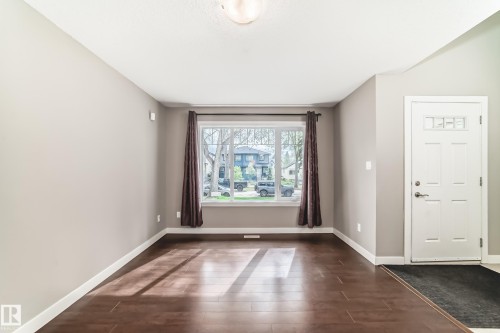 Bright living space featuring wood-finish flooring, neutral wall tones, a large picture window, and a white paneled entry door - 12118 125 Street Nw, Edmonton, AB - Indoor Photo Showing Other Room