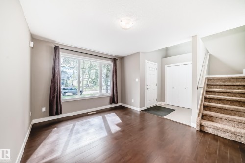 Wood-finish flooring throughout the main area, complemented by a large picture window with white trim - 12118 125 Street Nw, Edmonton, AB - Indoor Photo Showing Other Room