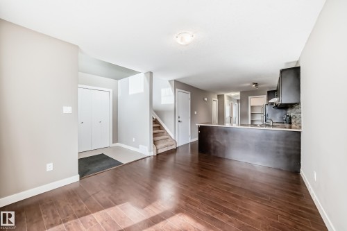 Open-concept living space featuring wood-finish flooring, a kitchen island with stone countertop, dark cabinetry, and a carpeted staircase - 12118 125 Street Nw, Edmonton, AB - Indoor