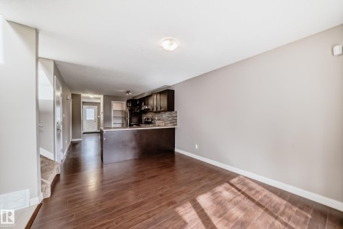 Spacious open-concept area featuring wood-finish flooring, a kitchen with dark cabinetry, a breakfast bar, and a tile backsplash - 12118 125 Street Nw, Edmonton, AB - Indoor Photo Showing Other Room