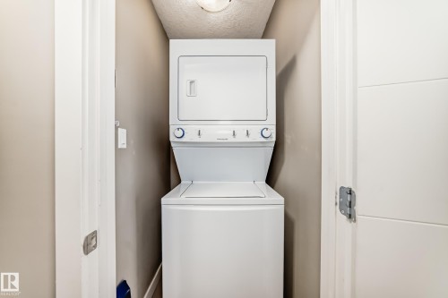 Dedicated laundry closet featuring a white stacked washer and dryer unit, neutral wall paint, and overhead lighting - 12118 125 Street Nw, Edmonton, AB - Indoor Photo Showing Laundry Room